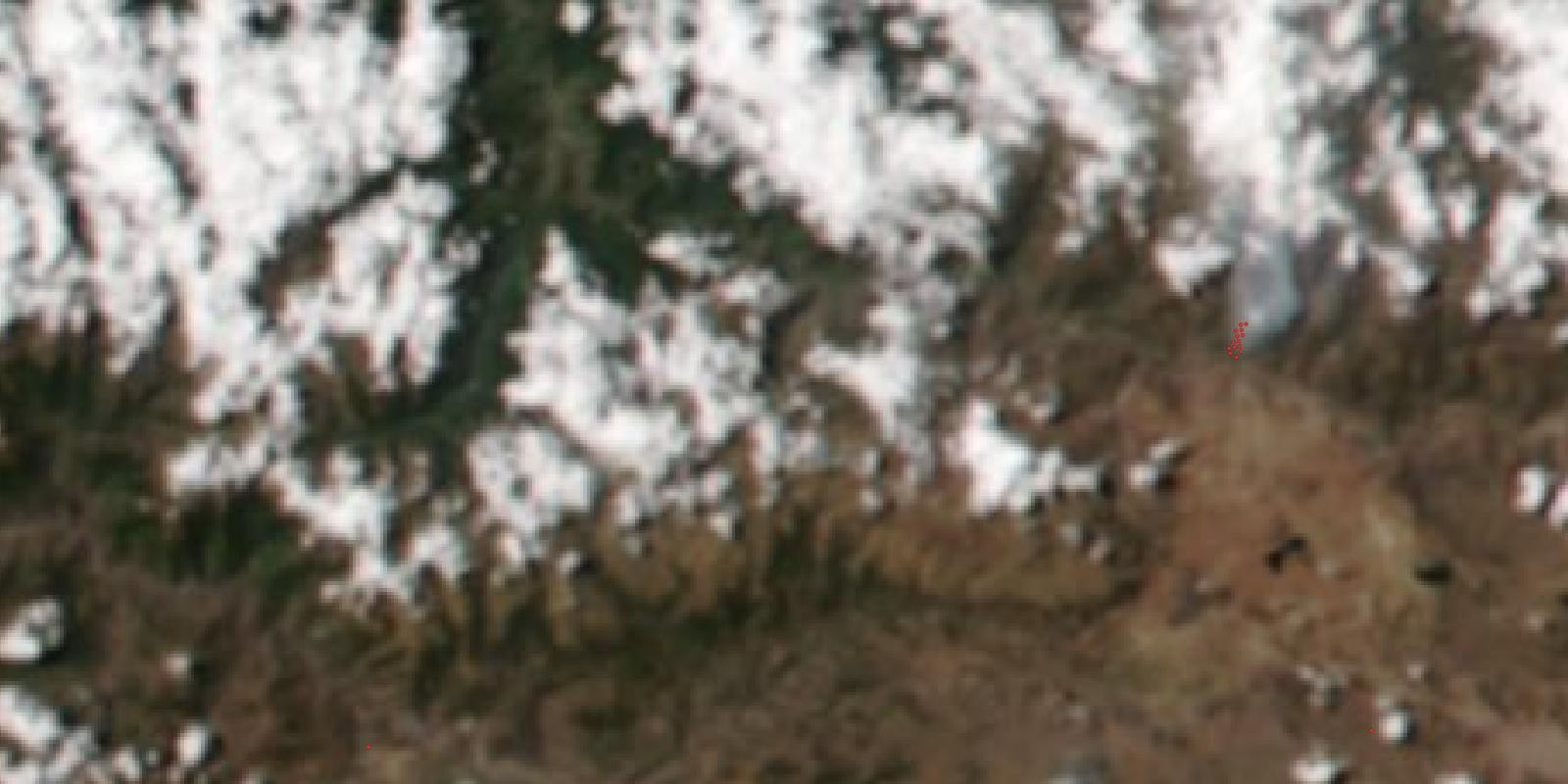 衛星から見た真色画像。褐色の乾いた山地に白い雲が点在し、画面右寄りに赤い小さな点の集まりと、そこから北へ流れる灰白色の煙の帯が写っている